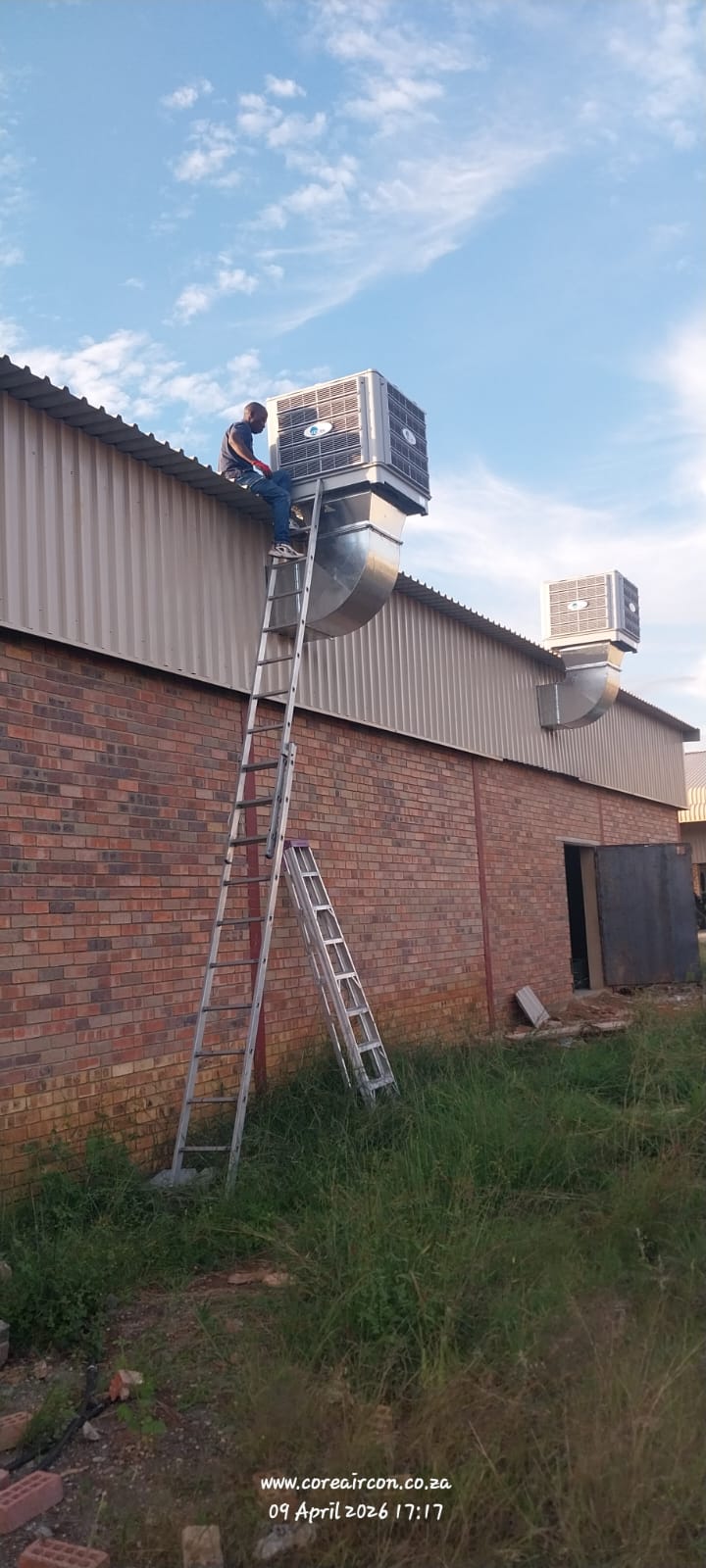 Technician installing evaporative cooling duct on warehouse roof